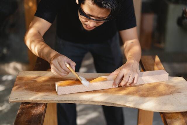 person painting a piece of wood and wearing safety glasses